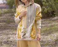Canguro con capucha y cierre frontal, color beige con estampado de hojas en tonos marrones y amarillos. Mangas largas en color gris.