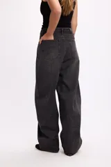 Pantalón de jean estilo baggy, de corte amplio y tiro medio, confeccionado en denim negro con textura de pana fina. Presenta diseño de cinco bolsillos, cierre frontal con botón metálico y cremallera, y perneras holgadas.