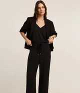 Pantalón femenino negro, modelo wide leg, de cintura alta con cordón ajustable y lazo. Presenta textura arrugada característica del tejido crepé airflow y bolsillos laterales.