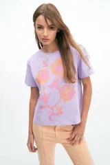 Remera lila de algodón con estampado de flores en tonos naranja y rosa. De corte recto y manga corta.
