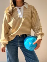 Buzo tipo chomba de corte oversize con diseño a rayas horizontales celestes y blancas. Presenta cuello camisero blanco y un bordado en la espalda con la inscripción República Oriental del Uruguay.