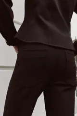 Pantalón flare de tiro bajo color marrón oscuro, con bolsillos delanteros y traseros, pierna entallada y bajo acampanado. Cierre frontal con cremallera y botón.