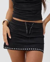 Minifalda negra de gamuza con cordones frontales decorativos y detalle de tachas plateadas en el ruedo.