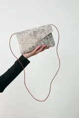 Bandolera pequeña de diseño minimalista en color plateado metalizado con acabado texturizado. Cuenta con cierre de solapa y cordón de cuero fino extraíble que permite su uso como sobre.