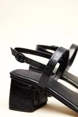 Sandalia de cuero vacuno color negro con textura de cocodrilo, taco cuadrado de 4 cm, punta cuadrada y dos tiras finas, una en el empeine y otra con hebilla en el tobillo.