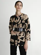 Saco acolchado con estampado abstracto en negro y beige, cuello redondo, cierre con botones a presión y bolsillos laterales. Incluye cinturón ancho de cuero negro con hebilla rectangular.