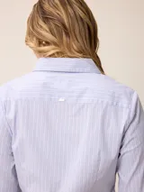 Camisa de corte clásico y calce entallado, color blanco, con cuello camisero, cierre frontal de botones y mangas largas con puños abotonados. Presenta un pequeño bordado distintivo en el pecho.