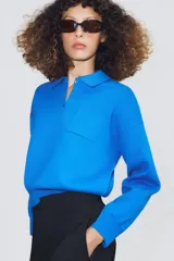Jersey de punto con cuello tipo polo, manga larga con puños y cierre frontal con botones. Presenta un bolsillo de plastrón en el pecho y diseño de corte holgado.