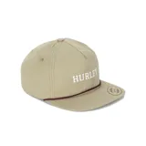 Gorra tipo trucker color oliva, con visera plana, cordón decorativo marrón sobre la base de la visera y el nombre de la marca 'HURLEY' bordado en blanco en el frente.