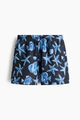 Short de baño azul marino con estampado de peces, estrellas de mar y caracolas en tonos azules y blancos. Cuenta con cintura elástica con cordón de ajuste.