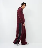 Pantalón de jogging color bordó con paneles laterales en negro y detalles de líneas blancas. Presenta un corte holgado y cintura elástica con cordón de ajuste.