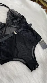 Body de encaje y microtul negro con diseño de escote halter, espalda descubierta y cierre con ganchos. Presenta paneles de encaje floral y secciones de tul transparente.