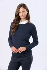 Buzo tejido en hilo de algodón color beige, con cuello redondo y manga larga. Presenta un corte clásico y un pequeño detalle metálico en la parte inferior izquierda.