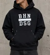 Canguro negro de corte oversize con capucha, estampado frontal con letras blancas y detalle de tachas metálicas en el borde de la capucha y el bolsillo frontal.