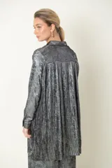 Camisa plateada de poliéster con textura metalizada, corte amplio, cuello clásico, cierre frontal con botones y mangas largas con puños abotonados.