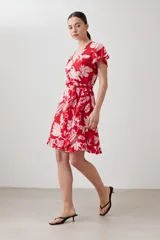 Vestido corto cruzado de color rojo con estampa floral blanca, con volados en el ruedo y lazo para ajustar en la cintura.