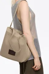 Bolso shopper mediano de tejido de punto color beige, con doble asa corta de mano y una correa larga ajustable para el hombro. Incluye parche con logo en la parte frontal.