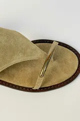 Sandalia plana de gamuza color tostado, con diseño de tira en T y argolla metálica en el empeine. Cuenta con tira ajustable con hebilla en el talón.