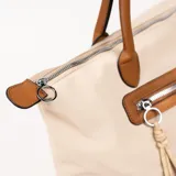 Bolso tipo tote color beige con detalles en marrón, cierre superior y bolsillo externo con cierre.