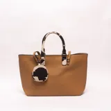 Cartera tipo tote de color marrón, con diseño texturizado, asas de mano con estampado de vaca y un monedero colgante redondo con el mismo estampado.