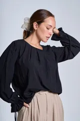 Blusa de manga larga color rosado, con cuello redondo y puños elásticos con volados y lazos decorativos. Presenta un diseño holgado con frunces en el escote.