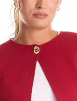 Cardigan tejido de punto color beige, con cuello a la base y cierre frontal mediante un botón metálico decorativo. Presenta mangas largas y corte recto.