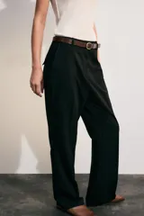 Pantalón de tiro alto color negro, de corte recto y pinzas frontales. Incluye un cinturón delgado de cuero marrón con hebilla metálica dorada.