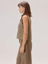 Chaleco negro sin mangas, de corte recto y largo a la cintura, con cuello redondo y cierre frontal oculto.