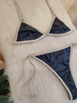 Conjunto de bikini negro con elástico tostado. El corpiño es de corte triangular con breteles regulables y aro metálico en el centro. La bombacha es tipo colaless con tiras laterales regulables.