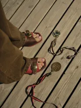 Sandalias de cuero con tiras anchas en color negro y beige, con un detalle circular metálico en el centro. La suela tiene un borde trenzado en blanco y negro.