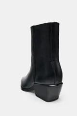 Botín de cuero negro estilo cowboy, con tacón medio ancho y punta fina. Cuenta con cierre mediante cremallera lateral.