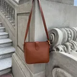 Cartera tipo morral de eco cuero color marrón, con cierre superior y correa larga ajustable. Interior forrado con bolsillos organizadores.