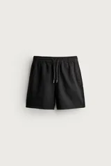 Bermuda de corte relajado color negro, confeccionada en tejido de algodón con textura. Cuenta con cintura elástica con cordón ajustable, bolsillos laterales y un pequeño bordado a tono en la pierna.