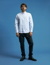 Camisa de corte clásico confeccionada en tejido oxford, con diseño de rayas verticales en tonos azul y blanco. Presenta cuello abotonado, cierre frontal con botones y bolsillo en el pecho con detalle de etiqueta bordada.