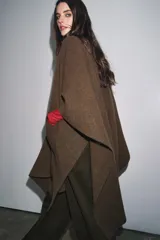 Capa de punto color marrón, con escote en V, mangas cortas y bolsillos de plastrón en el delantero. El ruedo tiene un corte asimétrico.