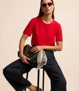 Blusa blanca de poliéster con cuello redondo, mangas cortas, cierre trasero en forma de gota, pequeñas aberturas laterales y acabados en pespuntes en las mangas y el cuello.