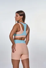 Conjunto deportivo de dos piezas compuesto por un top y un short de tiro alto. El top presenta un diseño de bloques de color en salmón y celeste con escote redondo y espalda deportiva. El short es de corte ajustado, con paneles laterales en contraste de color y textura acanalada.