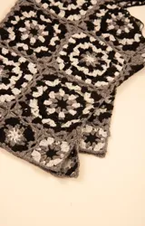 Polera sin mangas tejida en crochet con diseño de motivos cuadrados en tonos blanco, negro y gris. Presenta cuello cuadrado y breteles anchos.