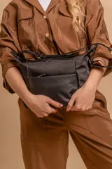 Bandolera de diseño práctico con combinación de texturas en tonos tierra, confeccionada en tela y símil cuero. Cuenta con un compartimento principal con cierre, un bolsillo frontal con cierre y correa ajustable para llevar al hombro o cruzada.