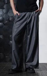 Pantalón sastrero de corte oversize en color gris, confeccionado en tejido premium con caída estructurada. Presenta dos pinzas frontales profundas, cintura ancha, bolsillos laterales y bolsillos traseros tipo ojal. Incluye detalles de botones en el ruedo.