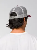 Gorro trucker Caterpillar color bordó con parte trasera de red gris, visera curvada y logo bordado en relieve en el frente.