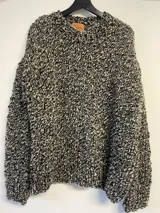 Sweater tejido a mano en lana gruesa color blanco y negro jaspeado, de calce holgado, cuello redondo y puños ajustados.