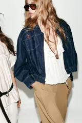 Chaqueta estilo bomber confeccionada en tejido denim azul oscuro. Presenta cuello solapa, cierre frontal con cremallera, mangas largas y bajo elástico. Incluye bolsillos delanteros de plastrón con solapa y botones.