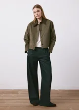 Chaqueta verde militar corta con cuello camisero de pana marrón oscuro, cierre frontal de botones, bolsillos aplicados en el pecho y diseño holgado.