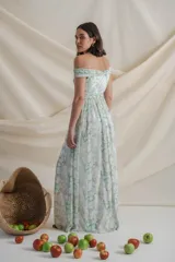 Vestido largo de gasa de seda natural estampada en tonos blanco, verde y amarillo. Diseño drapeado con escote barco y manga caída, falda con movimiento y tajo lateral.