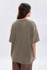 Remera de manga corta con corte oversize, color verde oliva con efecto de teñido especial. Presenta una estampa frontal en color blanco que simula un sello postal con motivos florales y la inscripción 'Fiori di Roma'.