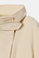 Trench de algodón con cuello alto, manga larga ajustable con trabillas y cierre frontal con botones ocultos. Presenta trabillas en los hombros, bolsillos laterales ocultos y cinturón ajustable en la cintura.