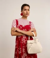 Cartera tipo bucket pequeña, color crudo, confeccionada en cuero sintético. Tiene doble asa, una corta de mano y otra larga para colgar al hombro. Se cierra con botón y tiene detalle de hebilla decorativa.