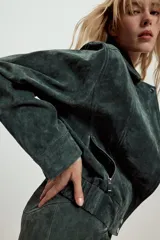 Cazadora de ante color verde oscuro, con cuello solapa, cierre frontal con cremallera oculta y botones a presión, bolsillos laterales con cremallera, manga larga con cremallera en puños y bajo elástico.