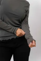 Remera de manga larga en tejido liviano y translúcido color gris oscuro, con cuello redondo y terminaciones onduladas en ruedo y puños.